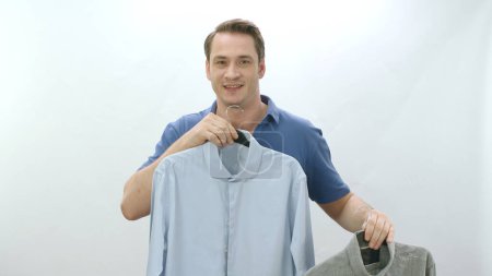 Photo for Young man isolated in front of white background holding two shirts. The man can't decide which shirt to wear. Not being able to decide on the choice of clothes. - Royalty Free Image