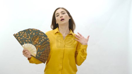 Photo for Young woman isolated on white background high temperature summer heat problem at home. Annoyed girl holding fan in hot weather. Stress in summer weather, sweating, heat problem. - Royalty Free Image