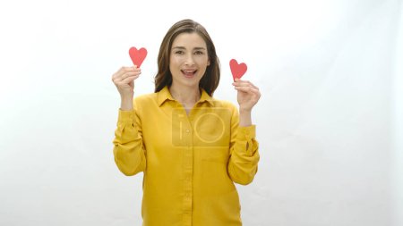 Photo for Smiling young woman isolated on white background dancing with two paper hearts she made. Portrait of a smiling woman with two paper hearts. Valentine's or mother's day celebration. - Royalty Free Image