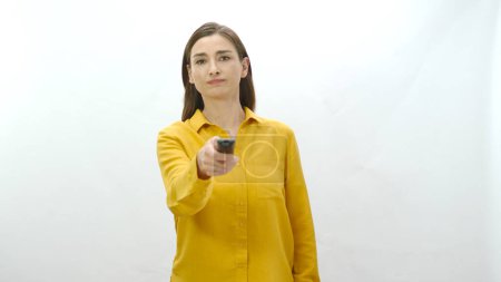 Woman holding tv remote control in hand isolated on white background. The woman searches for the program she wants to watch on television channels. Undecided woman portrait.