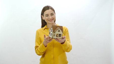Photo for Character portrait of young woman holding a model of her newly bought or rented house. Examines the House Model and shows it to the camera. The young woman draws attention to the housing crisis. - Royalty Free Image