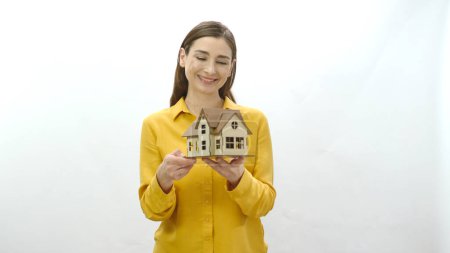 Portrait de caractère d'une jeune femme tenant un modèle de sa maison nouvellement achetée ou louée. Examine le modèle de la maison et le montre à la caméra. La jeune femme attire l'attention sur la crise du logement.