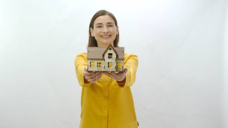 Photo for Character portrait of young woman holding a model of her newly bought or rented house. She examines the model and shows it to the camera. The young woman draws attention to the housing crisis. - Royalty Free Image