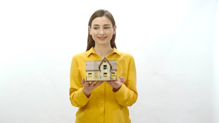 Junge Frau mit einem Modell ihres neu gekauften oder gemieteten Hauses. Die Frau untersucht das Modell des Hauses, blickt auf die leere Werbefläche und lenkt die Aufmerksamkeit auf die Wohnungskrise.