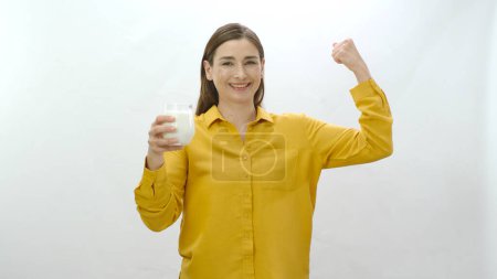 Téléchargez les photos : Portrait de caractère d'une jeune femme montrant ses biceps forts alors qu'elle boit du lait. Une femme qui dit être forte en buvant du lait. Isolé sur fond blanc. - en image libre de droit