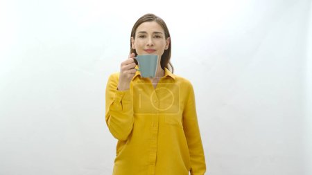 Charakterporträt einer jungen Frau, die eine Tasse Kaffee, schwarzen oder grünen Tee trinkt. Junge gesunde Frau schnüffelt Tasse Kaffee oder Tee isoliert auf weißem Hintergrund und zeigt in die Kamera