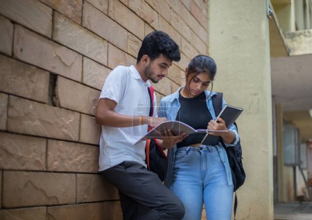 Téléchargez les photos : Amis étudiants universitaires de différentes ethnies tenant un livre et discutant de leurs études sur le campus. - en image libre de droit