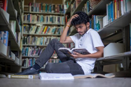 Photo for Young college student reading book time in the library, mature male with a book in his hands sitting on the floor near the bookcase, enjoying reading. Hobby concept - Royalty Free Image