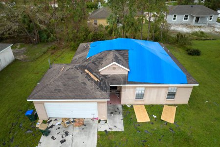 Hurricane Ian damaged house rooftop covered with protective plastic tarp against rain water leaking until replacement of asphalt shingles. Aftermath of natural disaster.