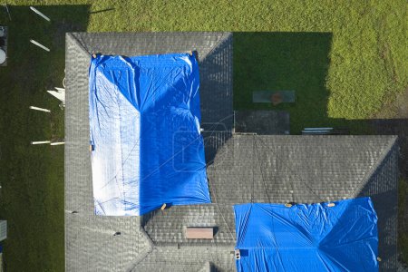 Draufsicht auf undichtes Hausdach mit schützenden Planen gegen undichtes Regenwasser bis zum Austausch von Asphaltschindeln abgedeckt. Schäden am Hausdach nach Hurrikan Ian in Florida.