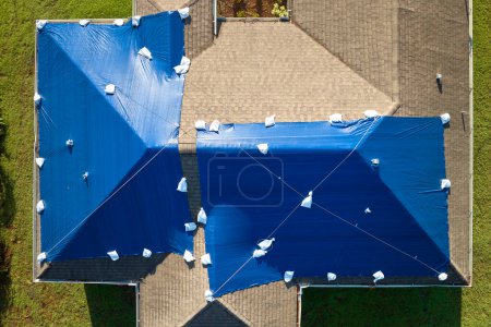 Vue aérienne du toit endommagé de la maison de l'ouragan Ian recouvert d'une bâche de protection bleue contre les fuites d'eau de pluie jusqu'au remplacement des bardeaux d'asphalte.