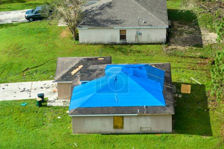 El huracán Ian dañó la azotea de la casa cubierta con lona plástica protectora contra fugas de agua de lluvia hasta la sustitución de las tejas de asfalto. Consecuencias de un desastre natural.