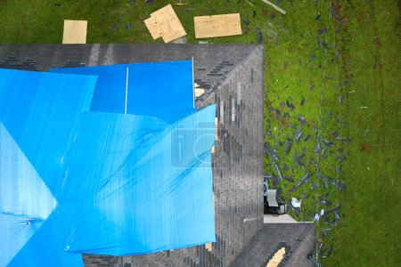 Aerial view of damaged in hurricane Ian house roof covered with blue protective tarp against rain water leaking until replacement of asphalt shingles.