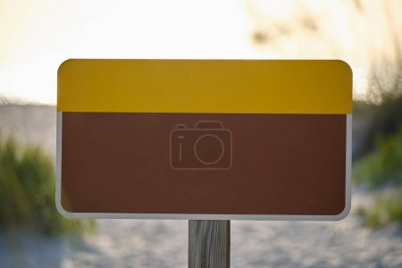 Empty signboard with copy space on seaside beach with small sand dunes and grassy vegetation on warm summer evening.