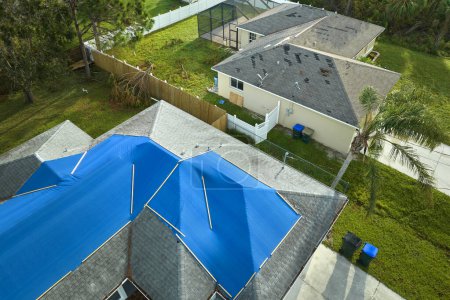 Draufsicht auf undichtes Hausdach mit schützenden Planen gegen undichtes Regenwasser bis zum Austausch von Asphaltschindeln abgedeckt. Schäden am Hausdach nach Hurrikan Ian in Florida.