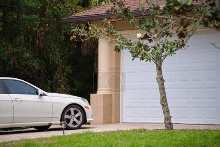 Photo for Vehicle parked in front of wide garage double door on paved driveway of typical contemporary american home. - Royalty Free Image