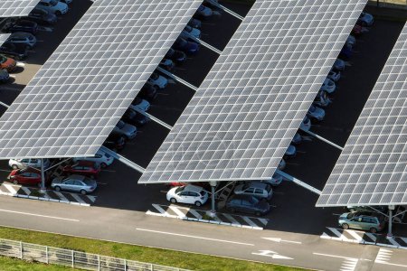 Aerial view of solar panels installed as shade roof over parking lot with parked cars for effective generation of clean electricity. Photovoltaic technology integrated in urban infrastructure.