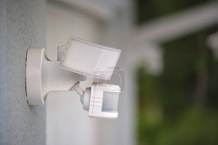 Motion sensor with light detector mounted on exterior wall of private house as part of security system.