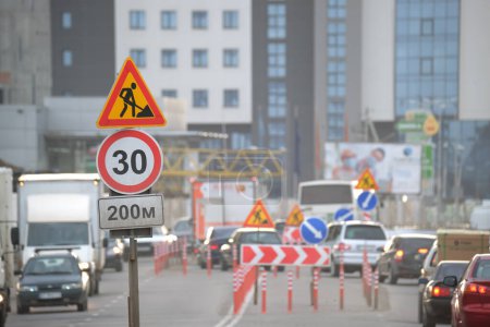 Photo for Roadworks warning traffic signs of construction work on city street and slowly moving cars. - Royalty Free Image