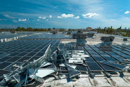 Top view of destroyed by hurricane Ian photovoltaic solar panels mounted on industrial building roof for producing green ecological electricity. Consequences of natural disaster in Florida.