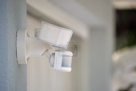 Motion sensor with light detector mounted on exterior wall of private house as part of security system.