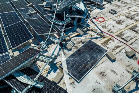 Aerial view of damaged by hurricane wind photovoltaic solar panels mounted on industrial building roof for producing green ecological electricity. Consequences of natural disaster.