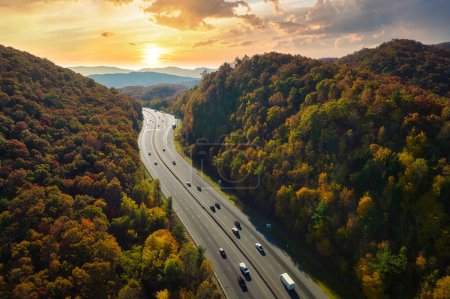Aerial view of I-40 freeway in North Carolina leading to Asheville through Appalachian mountains in golden fall with fast moving trucks and cars. Interstate transportation concept.