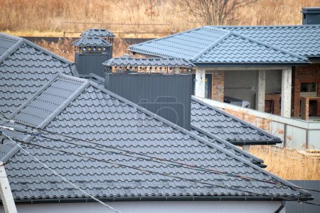 Schornstein auf Hausdach mit Metallschindeln im Bau. Fliesenverkleidung des Gebäudes. Immobilienentwicklung.