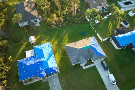 Téléchargez les photos : Vue du dessus des toits des maisons qui fuient et qui sont recouverts de bâches de protection contre les fuites d'eau de pluie jusqu'au remplacement des bardeaux d'asphalte. Dommages au toit de la construction à la suite de l'ouragan Ian en Floride. - en image libre de droit