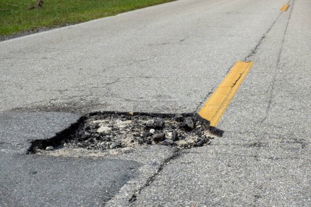 Pozo peligroso en la superficie de la carretera americana. Camino de entrada arruinado en necesidad urgente de reparación.