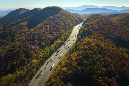 I-40 freeway road leading to Asheville in North Carolina over Appalachian mountain pass with yellow fall forest and fast moving trucks and cars. Concept of high speed interstate transportation.