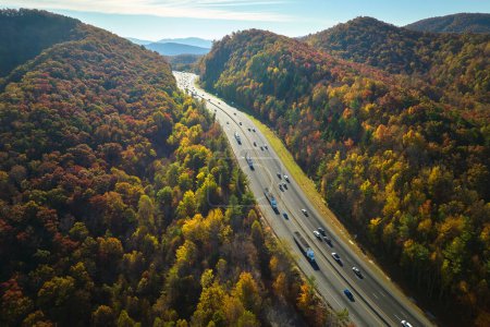Aerial view of I-40 freeway in North Carolina heading to Asheville through Appalachian mountains in golden fall with moving trucks and cars. Interstate transportation concept.