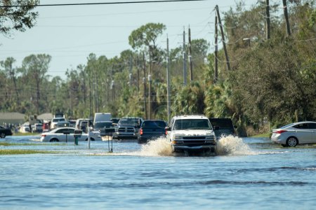 Flooded american street with moving vehicles surrounded with water in Florida residential area. Consequences of hurricane natural disaster.