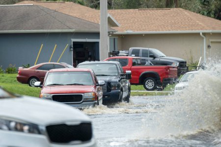 Hurricahe rainfall flooded Florida road with evacuating cars and surrounded with water houses in suburban residential area.