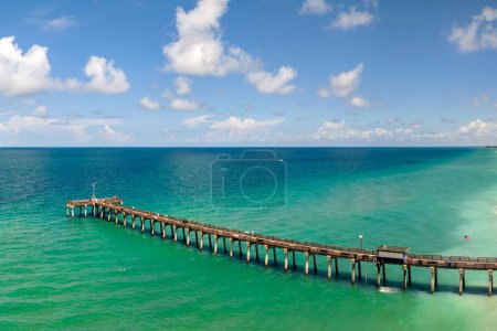 Venice fishing pier in Florida on sunny summer day. Bright seascape with surf waves crashing on sandy beach.