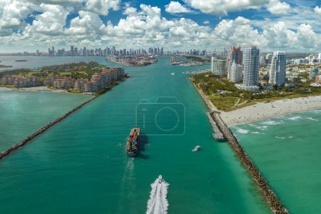 View from above of big container ship entering main channel in Miami harbor near South Beach high luxurious hotels and apartment buildings.