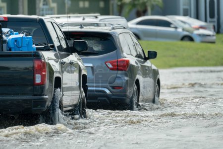 Photo for Hurricahe rainfall flooded Florida road with evacuating cars and surrounded with water houses in suburban residential area. - Royalty Free Image