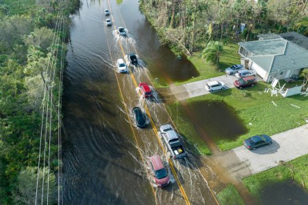 Hurricane flooded street with moving cars and surrounded with water houses in Florida residential area. Consequences of natural disaster.
