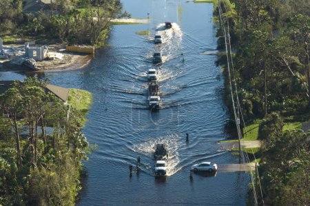 Foto de Inundada calle americana con vehículos en movimiento y rodeada de casas de agua en la zona residencial de Florida. Consecuencias del huracán desastre natural. - Imagen libre de derechos