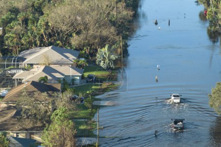 Flooded american street with moving vehicles and surrounded with water houses in Florida residential area. Consequences of hurricane natural disaster.