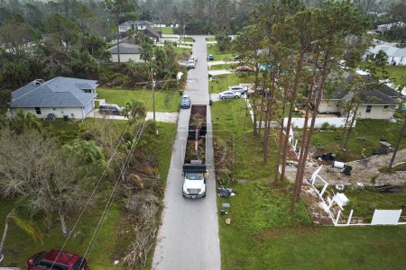 Téléchargez les photos : Vue aérienne de l'ouragan Ian après la récupération spéciale camion à benne basculante ramassant des débris de végétation des rues de banlieue de Floride. Faire face aux conséquences des catastrophes naturelles. - en image libre de droit
