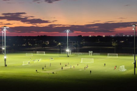 Menschen, die bei Sonnenuntergang ein Fußballspiel auf einem beleuchteten öffentlichen Stadion spielen. Konzept der aktiven Lebensweise.