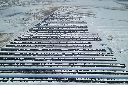 Aerial view of electrical power plant with solar panels covered with snow melting down in winter end for producing clean energy. Concept of low effectivity of renewable electricity in northern region.