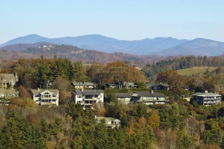 Vista aérea de grandes casas familiares en la cima de la montaña entre árboles amarillos en el área suburbana de Carolina del Norte en temporada de otoño. Desarrollo inmobiliario en suburbios americanos.