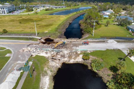 Repair of destroyed bridge after hurricane flood in Florida. Reconstruction of damaged road after flooding water washed away asphalt. Construction equipment at roadwork site.