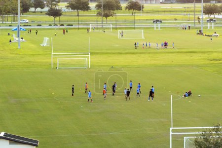 Téléchargez les photos : Vue aérienne du parc sportif public avec des enfants engagés dans un match de football sur le stade d'herbe au coucher du soleil. Concept de mode de vie actif. - en image libre de droit