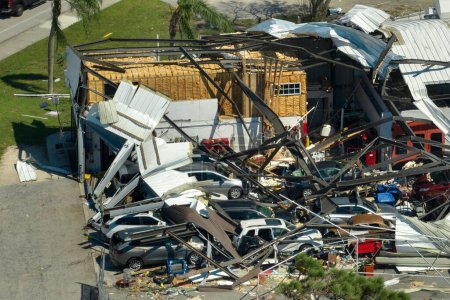Destroyed by hurricane industrial building with damaged cars under ruins in Florida. Natural disaster and its consequences.