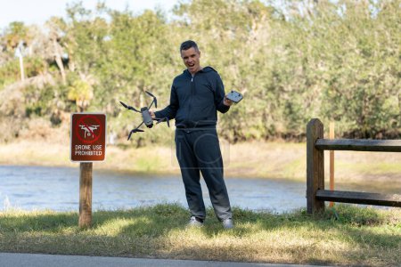 Drone operator is disappointed because he isnt allowed to fly his quadcopter in national park no drone area. Man is unable to use his UAV near restriction notice sign. Airspace use regulations.