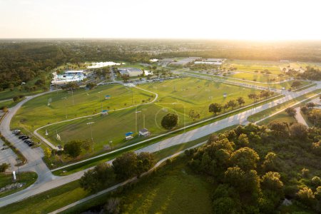 Illuminated public sports arena in North Port, Florida with people playing soccer game on grass football stadium at sunset. Outdoor activities concept.