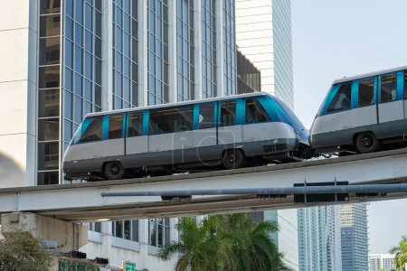 Public transportation in downtown Miami in Florida USA. Metrorail city train car on high railroad over street traffic between skyscraper buildings in modern American megapolis.
